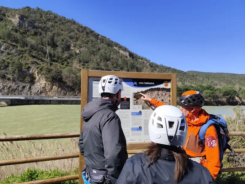 Grupo preparando la vía ferrata Pared de les Arcades junto al panel informativo